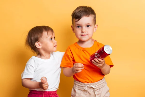 Vichuga. A Rússia. 27 de fevereiro de 2020: Irmão e irmã crianças felizes estão de pé com uma lata de Coca-Cola e um chupa-chupa em suas mãos. Os produtos contêm muito açúcar. — Fotografia de Stock