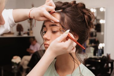 Güzellik salonunda çekim yapmak. Makyaj sanatçısı, göz farlarını kabarık bir fırçayla gözlerine sürer..