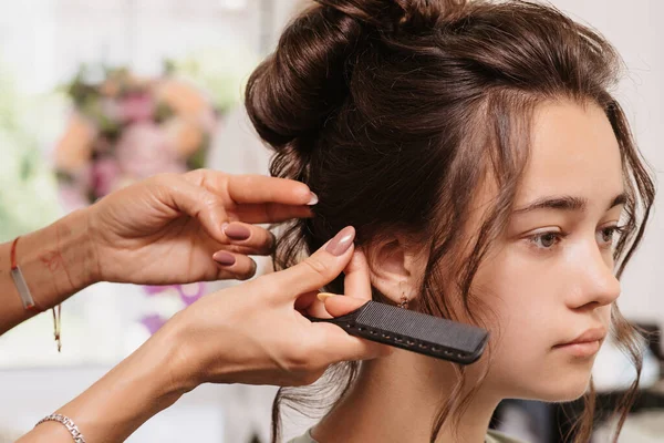 A filmar num salão de beleza. Um cabeleireiro corrige o penteado de uma jovem de cabelos escuros com um pente de cabelo. — Fotografia de Stock