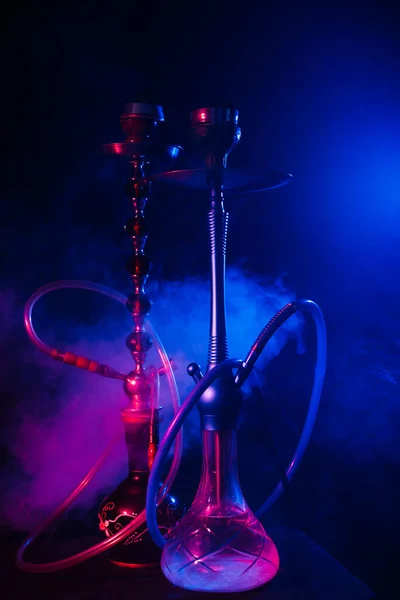 La cachimba a la moda con una nube de humo sobre un fondo negro con brillo rojo y azul — Foto de Stock