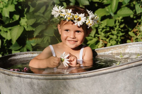 Un lindo bebé sonriente se está bañando en una bañera de pie en el jardín, en un día de verano soleado caliente —  Fotos de Stock