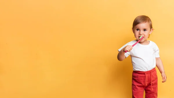 O conceito de higiene dentária. Uma menina loira escova os dentes com pasta de dentes. Fundo amarelo. Um lugar para o seu texto. — Fotografia de Stock