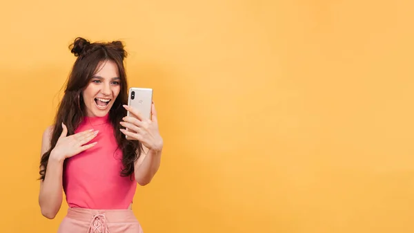 Uma mulher sorrindo segura um smartphone no qual ela grava uma mensagem de vídeo ou fala em um bate-papo por vídeo, de pé sobre um fundo amarelo. Uma cópia do espaço. Espaço para texto — Fotografia de Stock