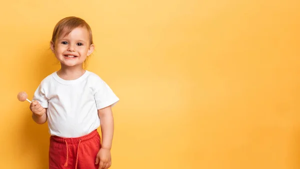 A menina está a comer um doce chupa-chupa num pau. Fundo amarelo. O conceito de prevenção de cárie e diabetes em crianças. Lugar para o seu texto — Fotografia de Stock