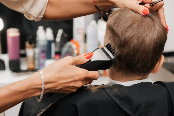 A filmar num salão de beleza. Um barbeiro faz um corte de cabelo para um menino com uma máquina — Fotografia de Stock