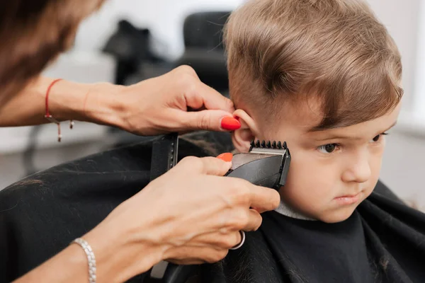 A filmar num salão de beleza. Um barbeiro corta o cabelo de um menino com uma máquina. — Fotografia de Stock