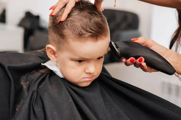Dreharbeiten in einem Schönheitssalon. Ein Friseur schneidet einem kleinen Jungen mit einer Maschine die Haare. — Stockfoto