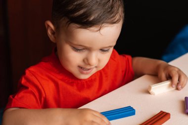 Bir çocuk masada oturan çok renkli plastiğin figürlerini yontuyor. Anaokulu eğitimi. Hobi olarak. Kendi kendini geliştirme