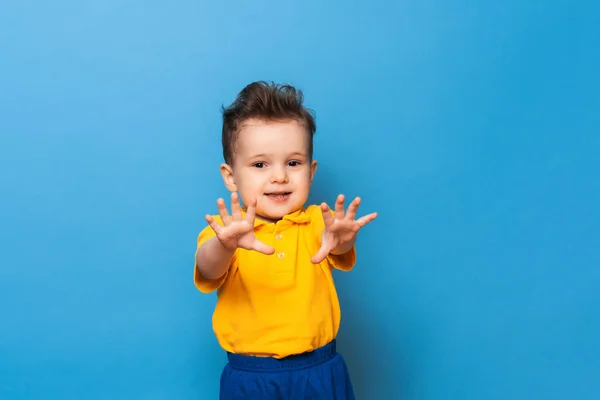 Cute little grimaces stoi na niebieskim tle. Zabawny dzieciak. — Zdjęcie stockowe