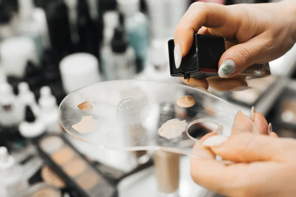 Uma mão de mulher segura uma paleta e espreme um produto cosmético, uma fundação, nela. close-up — Fotografia de Stock