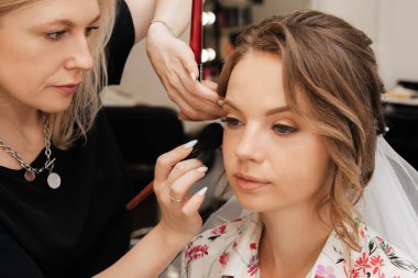 Güzellik salonunda çekim yapmak. Makyajcı genç bir kız için düğün makyajı yapıyor..