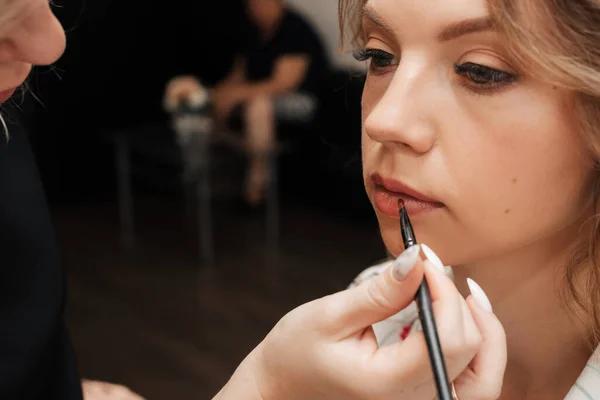 Schieten in een schoonheidssalon. make-up kunstenaar past make-up op een jong mooi meisje model — Stockfoto