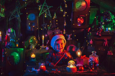 Muhteşem bir Noel atmosferi. Küçük bir çocuk, Noel Baba asistanı, hediyelerle masalarda. Yeni yıl süslemeleri. Kartpostal.