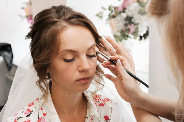A filmar num salão de beleza. artista de maquiagem aplica maquiagem para uma jovem noiva linda menina. — Fotografia de Stock