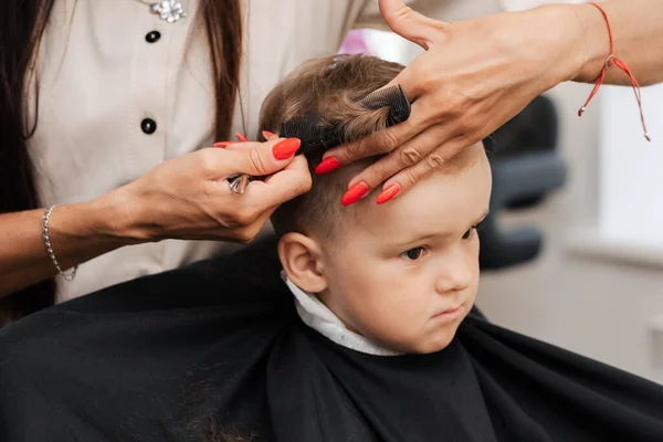 A filmar num salão de beleza. Um cabeleireiro dá um corte de cabelo a um menino com tesoura. — Fotografia de Stock