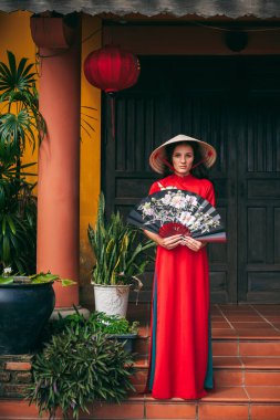 Geleneksel Vietnam kostümlü bir kadın, Hoi An 'ın antik bölgesinde elinde yelpaze olan konik bir şapka. Tet bayramı ve yeni yıl.