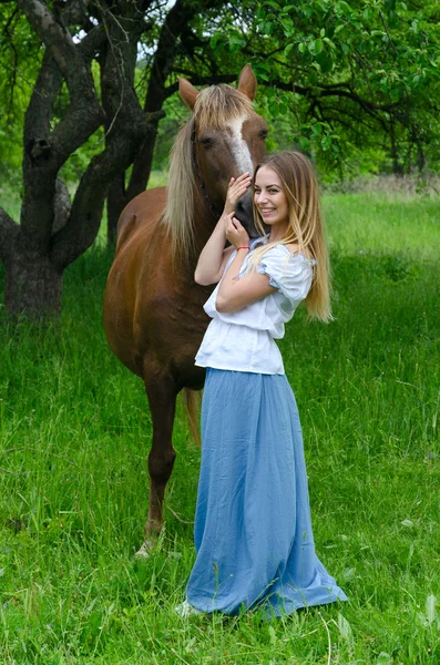 Красивая улыбающаяся девушка обнимает лошадь в яблоневом саду — стоковое фото