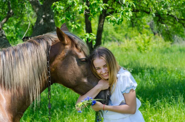 Beautiful girl embraces muzzle of chestnut horse and laughs — Stock Photo, Image