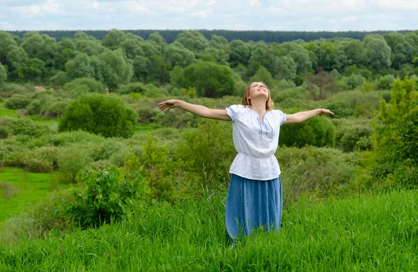 Menina feliz fica no fundo do campo com arbustos e olha para o céu — Fotografia de Stock