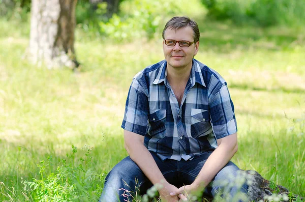 Glimlachende man zit op het gazon van bos op steen Rechtenvrije Stockfoto's