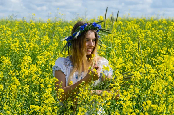 Beautiful girl in wreath of cornflowers on flowering rapeseed fi — Stock Photo, Image