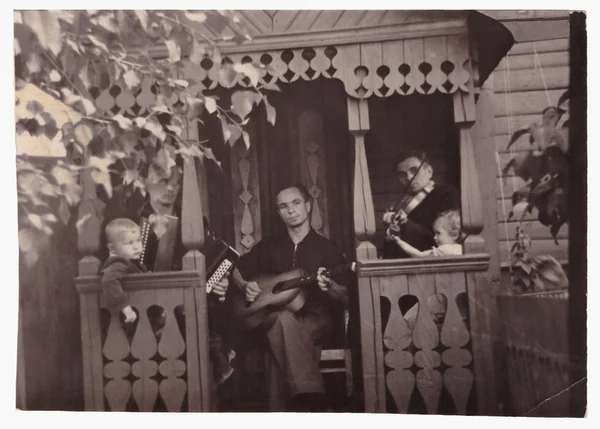 Trzech mężczyzn grać na instrumentach muzycznych w altance, w pobliżu domu (zdjęcie rocznika 1960) — Zdjęcie stockowe