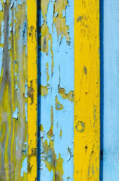 Fragment of wooden fence with cracked yellow and blue paint — Stock Photo, Image