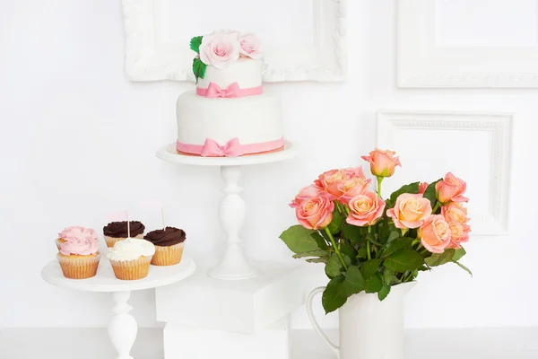 Cake decorated with roses and bows with cupcakes standing on a table — Stock Photo, Image