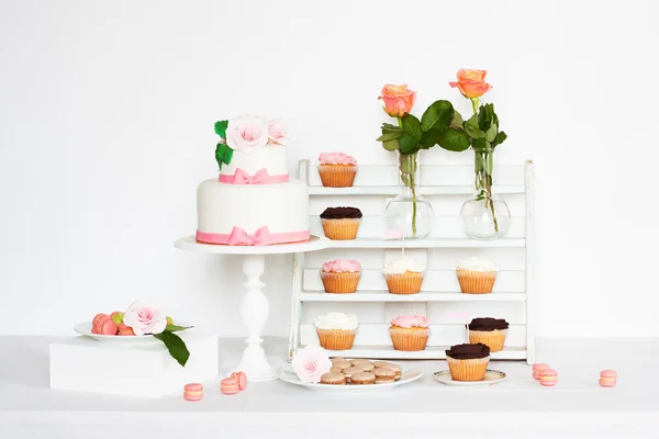 Cake decorated with roses and bows with cupcakes and macaroons standing on a table — Stock Photo, Image