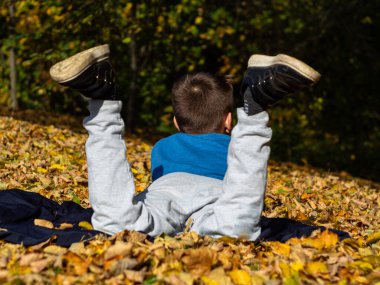 Oğlan bacak bacak üstüne atmış bir şekilde battaniyenin üzerinde yatıyor. Sonbahar Parkı 'nda sarı yapraklar. Ayakkabı tabanının arka görünüşü.