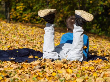Oğlan bacak bacak üstüne atmış bir şekilde battaniyenin üzerinde yatıyor. Sonbahar Parkı 'nda sarı yapraklar. Ayakkabı tabanının arka görünüşü.