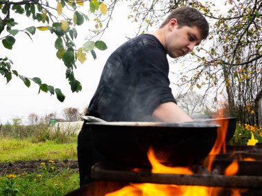Ateşin içinden fotoğraf çekmek. Bir adam yanan bir barbekü için yemek hazırlar. Kızartma tavasında ızgarada pişirmek