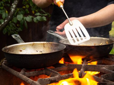 doğada piknik. Kızartma tavası yanıyor. Bir adam kızartma tavasında yemek pişiriyor.