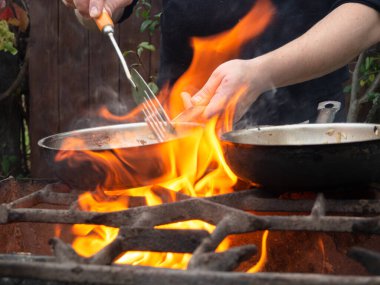 Kızartma tavasında ızgarada pişirmek. Kızartma tavası yanıyor. Bir adam kızartma tavasında yemek karıştırır.