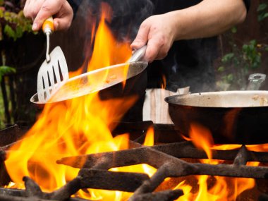 Kızartma tavasında ızgarada pişirmek. Kızartma tavası yanıyor. Bir adam kızartma tavasında yemek karıştırır.