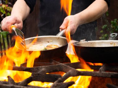 Kızartma tavasında ızgarada pişirmek. Kızartma tavası yanıyor. Bir adam kızartma tavasında yemek karıştırır.