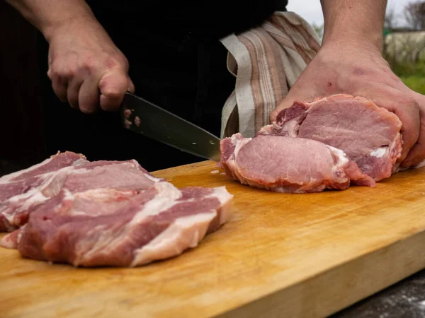 a man cuts meat steaks with a knife. boneless pork loin. dressed in a black apron with a towel on his belt