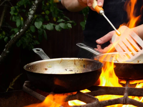 用煎锅在烤架上做菜 油锅着火了 一个人在煎锅里搅拌食物 — 图库照片