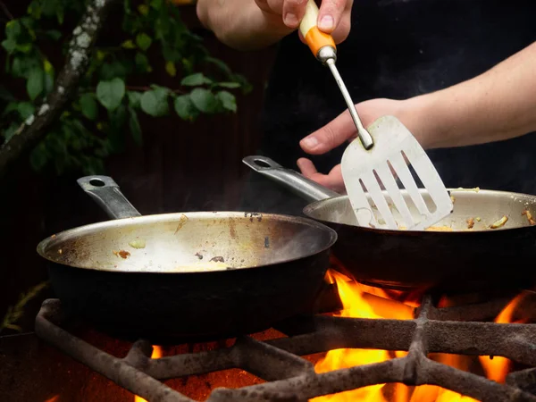 doğada piknik. Kızartma tavası yanıyor. Bir adam kızartma tavasında yemek pişiriyor.