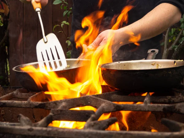 用煎锅在烤架上做菜 油锅着火了 一个人在煎锅里搅拌食物 — 图库照片