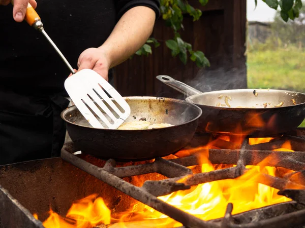 cooking on the grill in a frying pan. frying pan on fire. a man stirs food in a frying pan