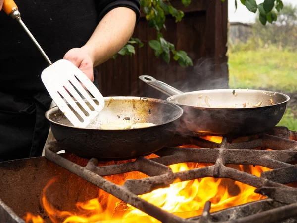 cooking on the grill in a frying pan. frying pan on fire. a man stirs food in a frying pan