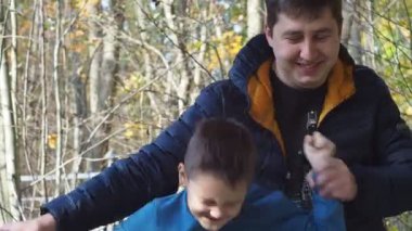 Baba oğul sonbahar parkında dans edip gülümsüyorlar. Samimi neşe ve mutluluk