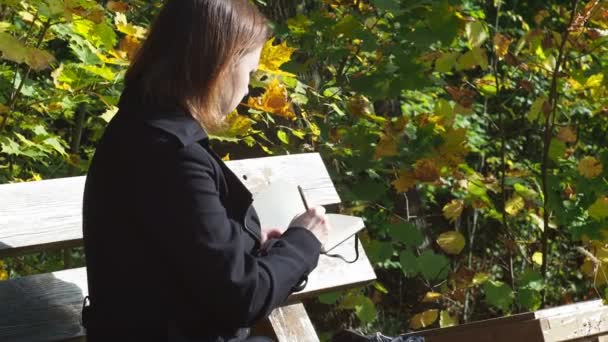 Nuori nainen piirtää luontoa kynällä istuessaan penkillä. taiteilija työssä — kuvapankkivideo