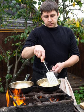 Bir adam ateşte tavada sebze kızartıyor. Kızartma tavasında kızarmış soğan..