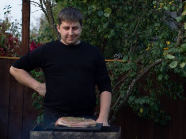 Siyah ceketli bir adam sokakta ızgarada biftek pişiriyor. Önlükle havluyla yemek pişirmek..