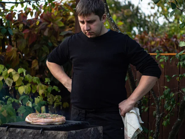 Mężczyzna Czarnej Kurtce Fartuchu Ręcznikiem Smażony Stek Grillu Podwórku — Zdjęcie stockowe