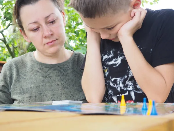 Annesi ve siyah tişörtlü bir çocuk masada bir küple oyun oynuyor..