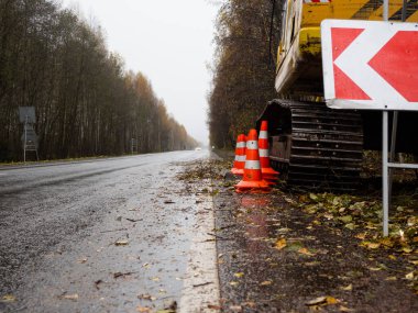 Sağdaki servis yolu tabelası. Yolun kenarında özel ekipman var. Yolda geçici trafik işaretleri var. Yolların onarımı.