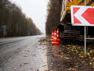 Sağdaki servis yolu tabelası. Yolun kenarında özel ekipman var. Yolda geçici trafik işaretleri var. Yolların onarımı.